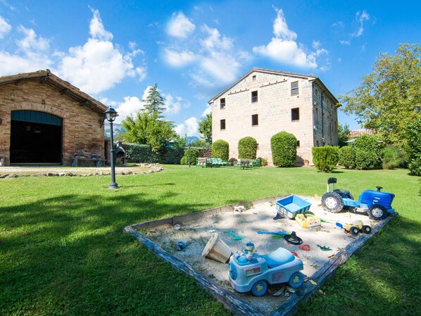 A backyard with a lawn, a wooden play area, and a stone building. - Belvilla by OYO Fattoria 19 (Amandola)