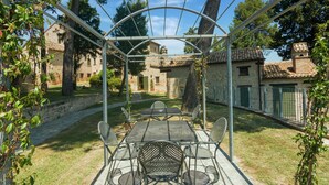 Un espace extérieur abrité, aménagé pour les repas, avec une pergola, des bâtiments en pierre et un mur de pierre en arrière-plan.