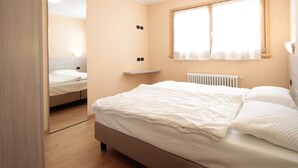 A bedroom with a bed, a mirror, a window with curtains, and a radiator. - Belvilla by Oyo Baita Morena Due Trilo (Livigno)