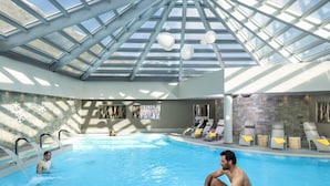 An indoor swimming pool with a glass ceiling, lounge chairs, and a stone wall. - Belvilla by Oyo Baita Morena Due Trilo (Livigno)
