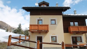 A two-story chalet with wooden balconies, a stone facade, and a clear view of the surrounding snowy landscape. - Belvilla by Oyo Baita Morena Due Trilo (Livigno)