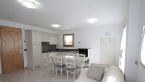 A modern kitchen with white cabinets, a dining area with a table and chairs, and a living room with a sofa. - Belvilla by Oyo Baita Morena Due Trilo (Livigno)