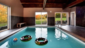 Une piscine intérieure avec des portes en verre transparent donnant sur un jardin.
