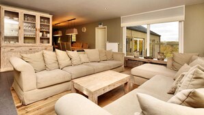 Un salon spacieux avec un grand canapé beige, une table basse en bois et un coin repas comprenant une table et des chaises en bois.