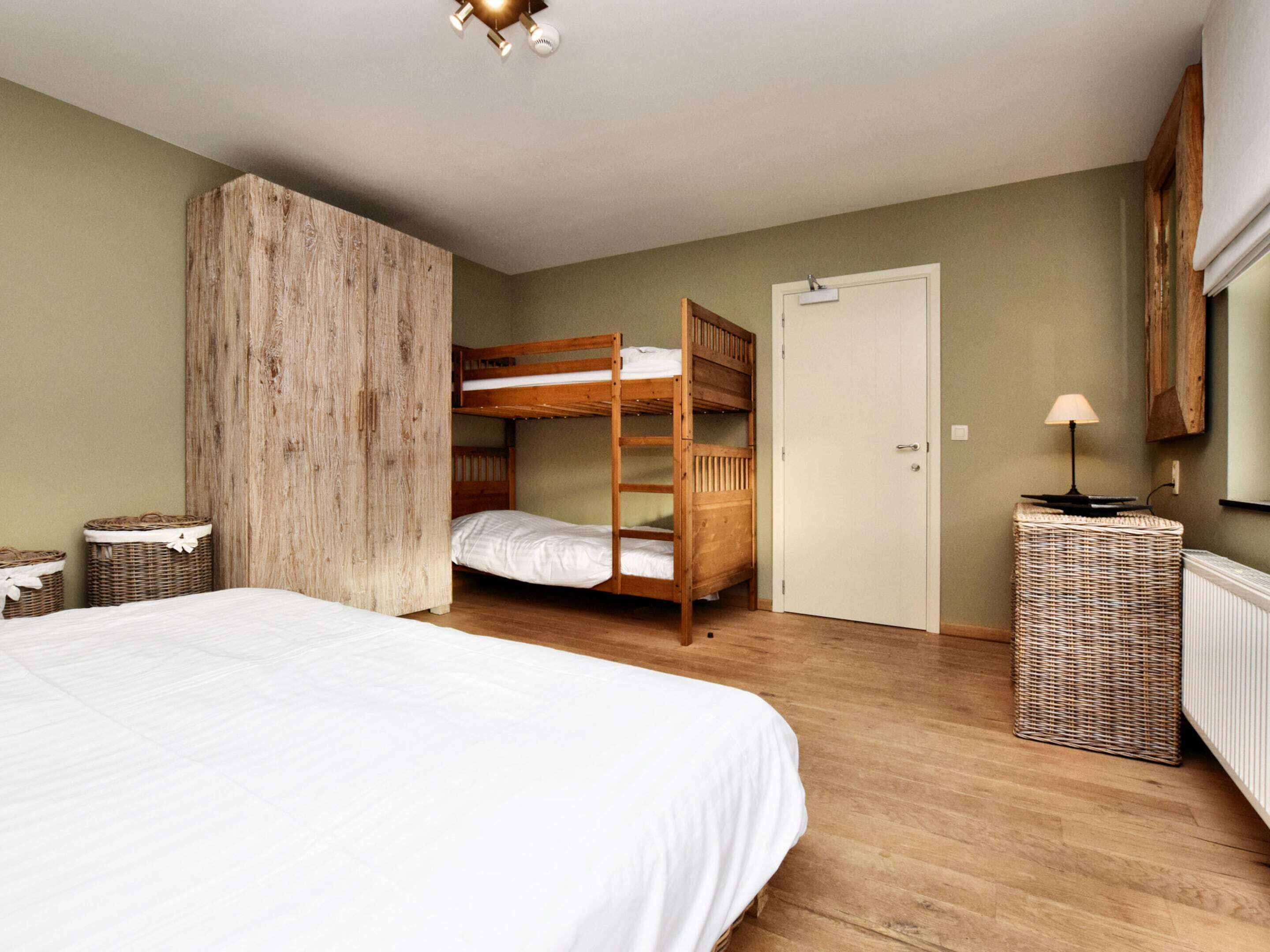 Une chambre avec un lit superposé, un lit simple, une armoire en bois, une table de chevet en osier et un radiateur.