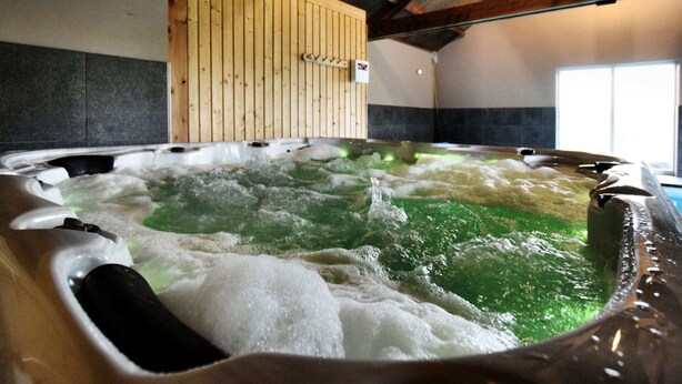 Un bain à remous avec de l’eau verdâtre, des murs en bois et un sol carrelé.