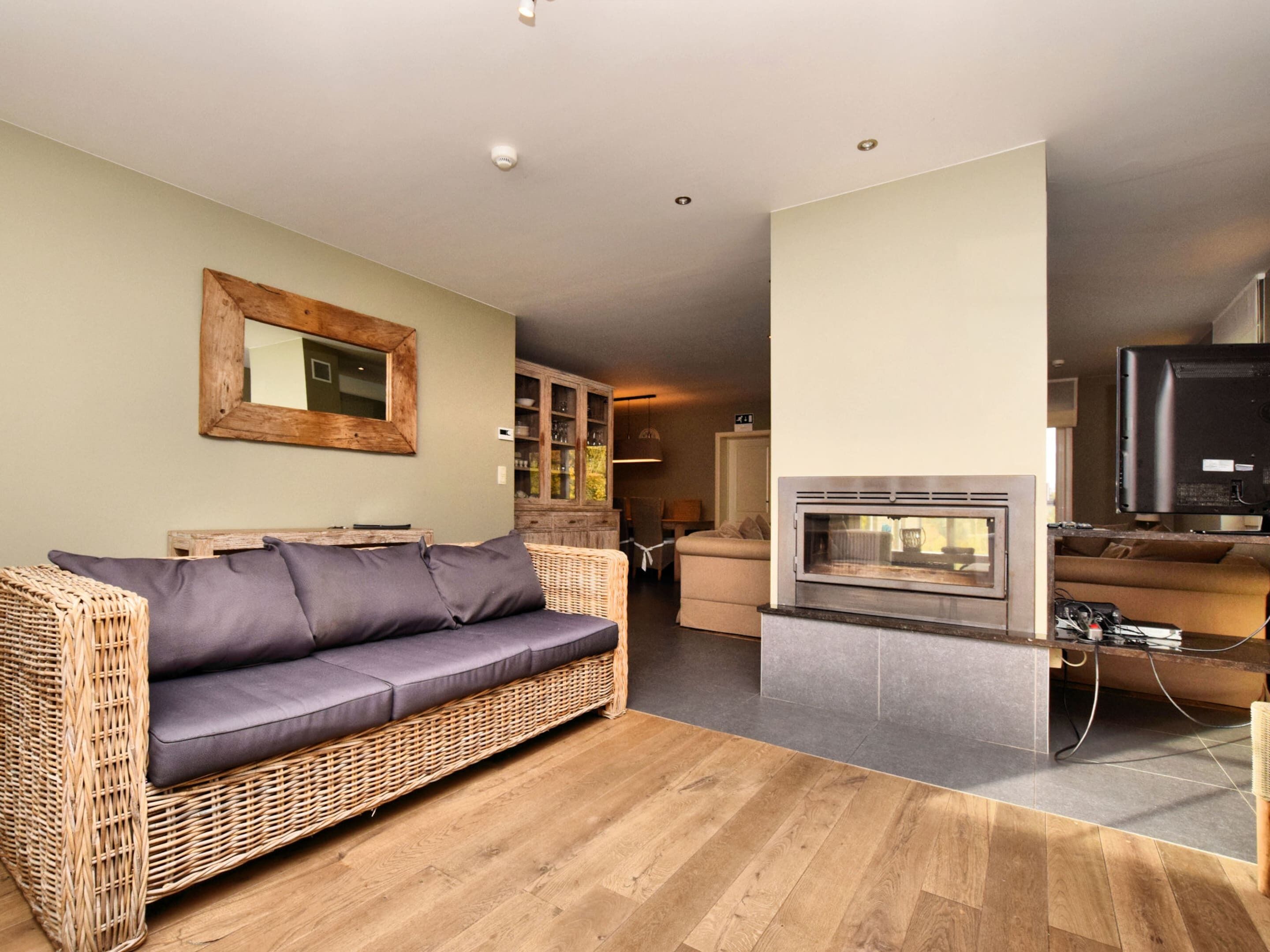 A living room with a wicker sofa, a fireplace, a television, and a dining area with a cabinet.