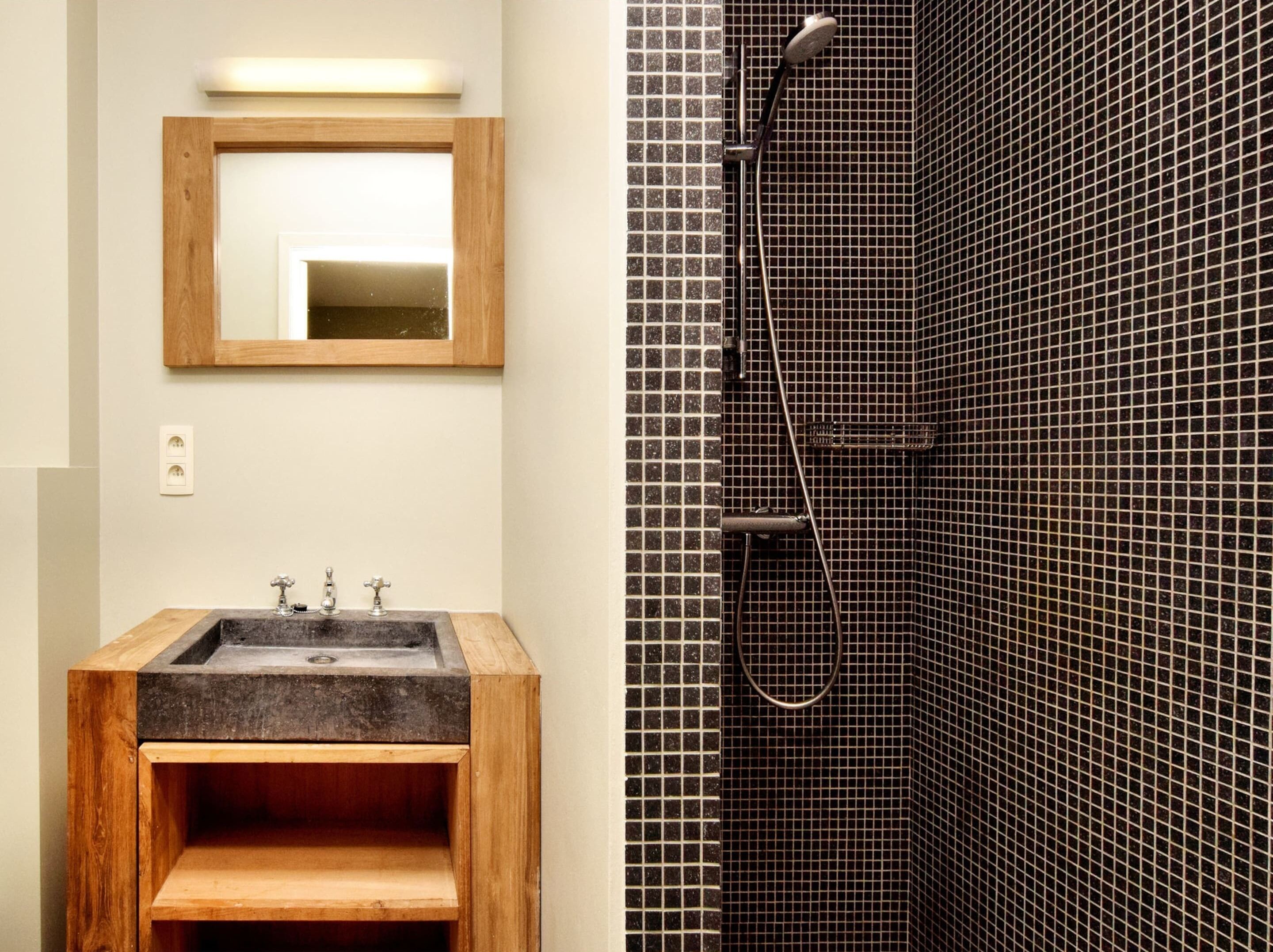 A bathroom with a wooden vanity, a mirror, and a shower with a tiled wall.