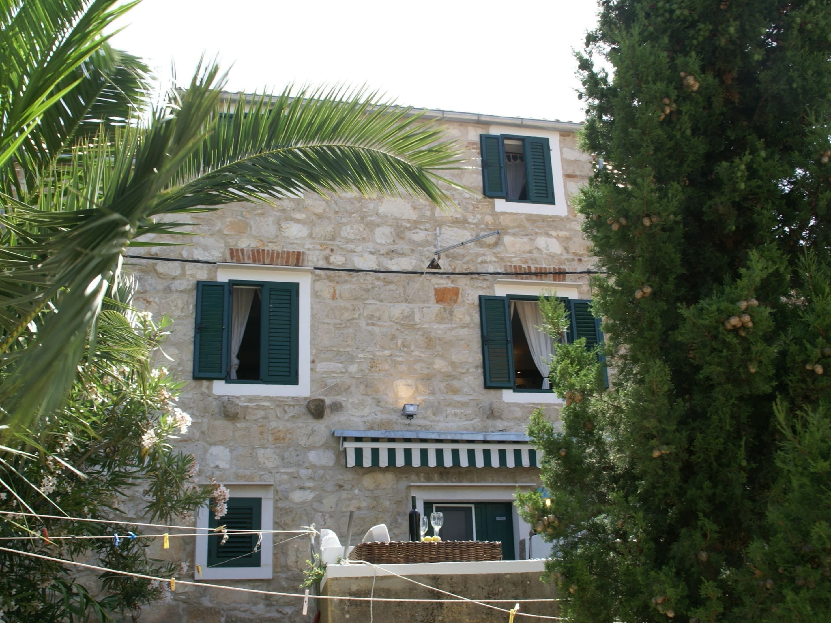 Un bâtiment en pierre avec des volets verts, un balcon orné d’un panier en osier et un fil à linge où sèchent des vêtements.