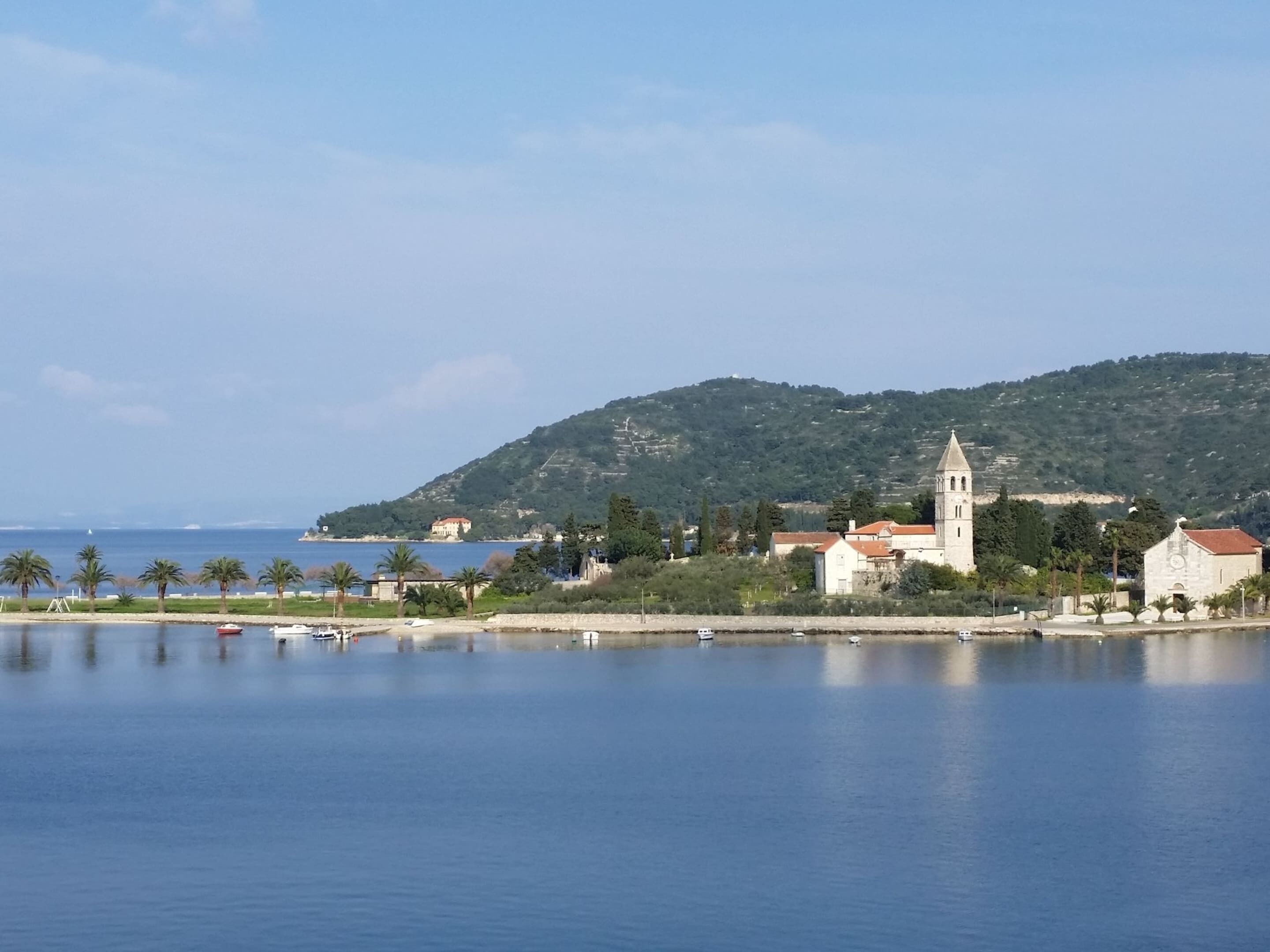 A coastal town with a prominent church, calm water, and a hilly backdrop.