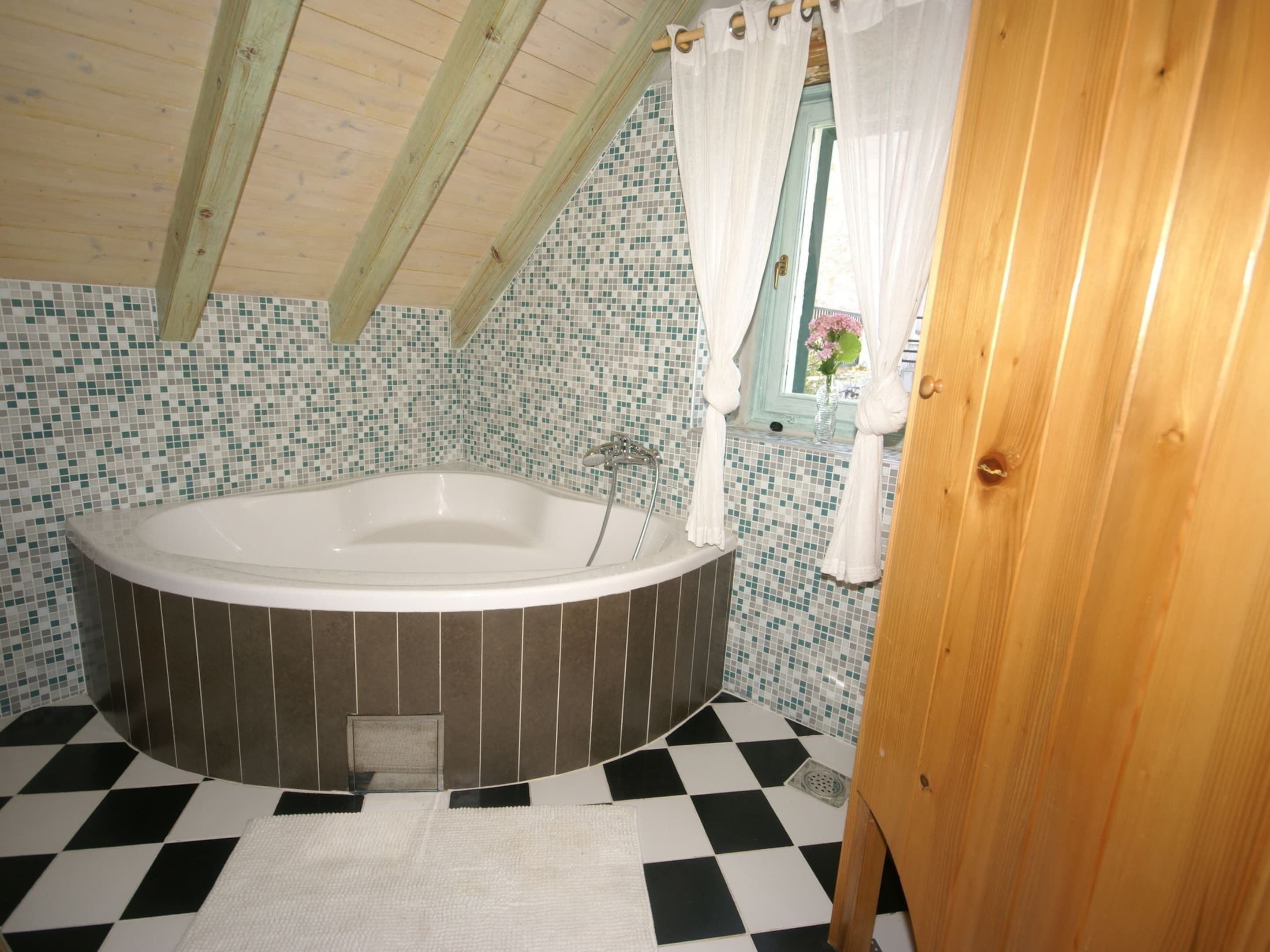 A bathroom with a freestanding bathtub, checkered floor tiles, and a mosaic tile wall.