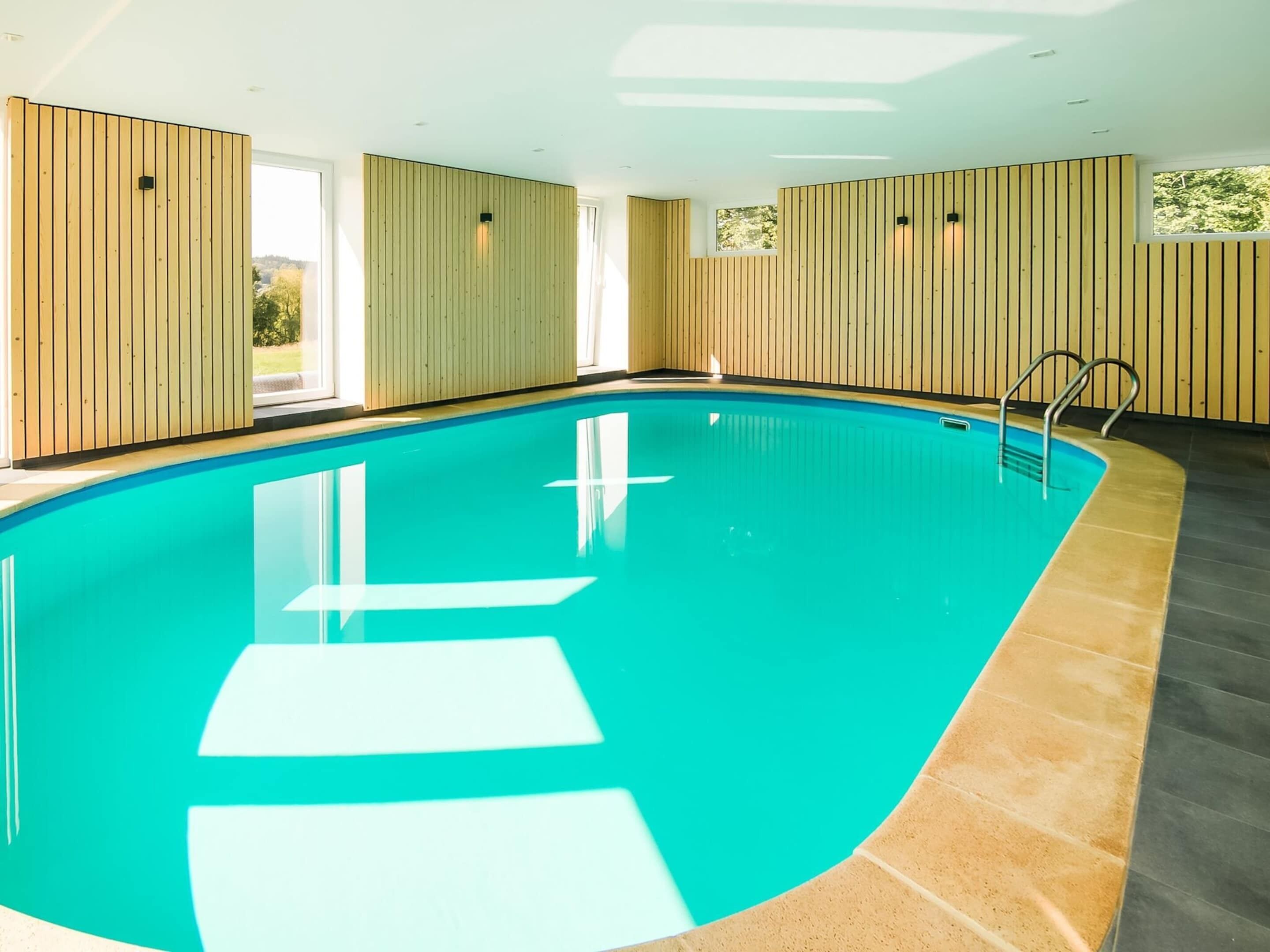 An indoor swimming pool with wooden panel walls, a tiled floor, and a metal ladder.