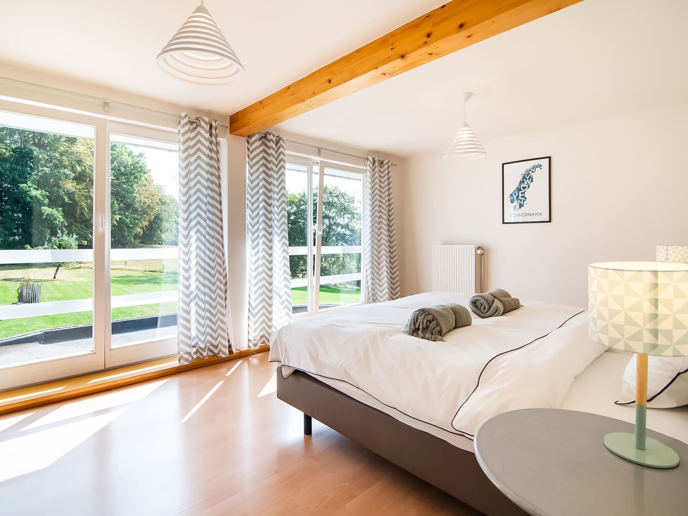 A bedroom with a bed, a bedside table, a lamp, and a window with curtains.