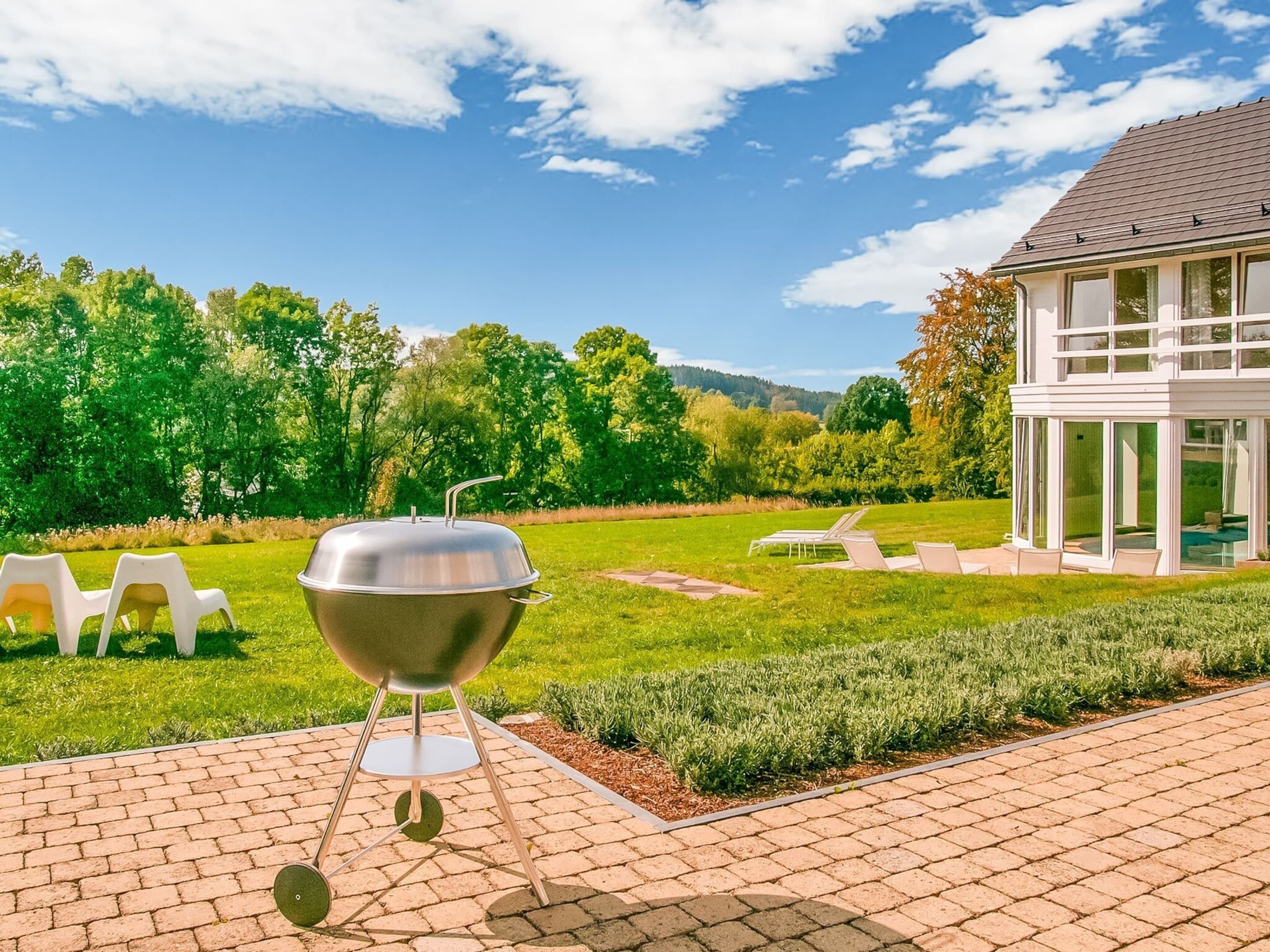 Una parrilla en un patio empedrado, con vistas a una casa y un área verde.