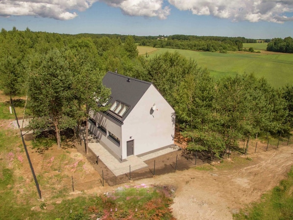 A modern house with a sloped roof, surrounded by trees and open fields.