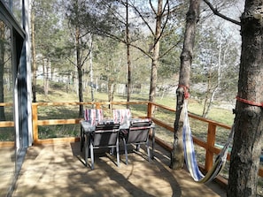 A wooden deck with a table and chairs, surrounded by trees and a hammock.