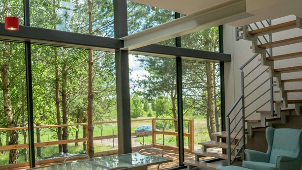 A modern interior with a glass table and chairs, a teal armchair, and a wooden staircase. - Glass Cottage in Jelenska Huta With Terrace (Szemud)