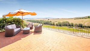 A patio with wicker furniture and a large umbrella, overlooking a scenic countryside. - Belvilla by OYO San Francesco Vermentino (Lajatico)
