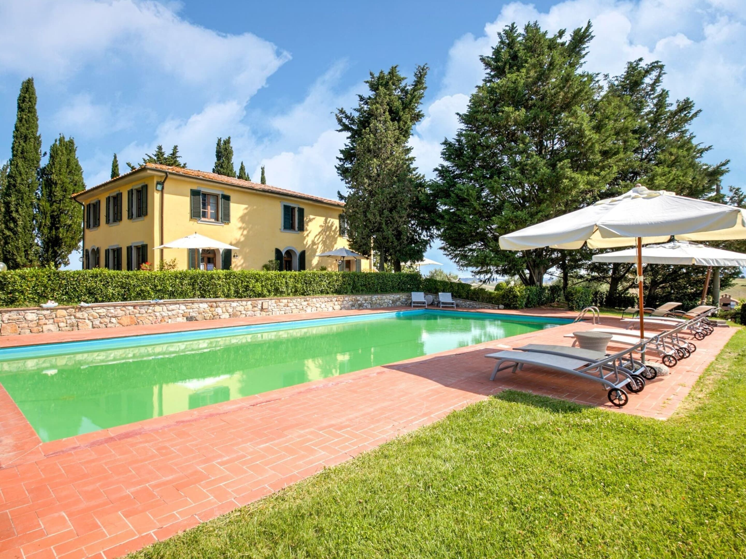 Una piscina con un sendero de ladrillos, sillas de descanso y sombrillas.