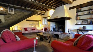 Ein gemütliches Wohnzimmer mit Kamin aus Stein, roten Sofas und Holzbalkendecke.