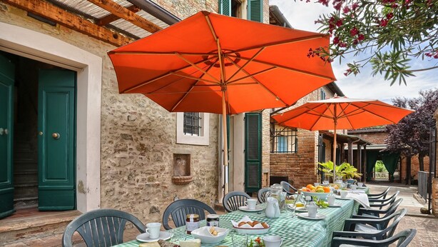 Un área de comedor al aire libre con manteles a cuadros, puertas verdes y sombrillas naranjas.