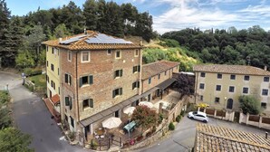 Un edificio de varios pisos con fachada de ladrillo, techo con paneles solares y un patio con mobiliario exterior.