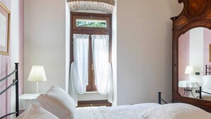 A bedroom with a bed, a nightstand, a lamp, a mirror, and a door with curtains. - Belvilla by OYO Vega (Caprino Veronese)
