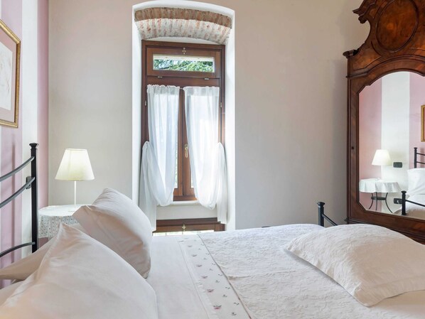 A bedroom with a bed, a nightstand, a lamp, a mirror, and a door with curtains. - Belvilla by OYO Vega (Caprino Veronese)