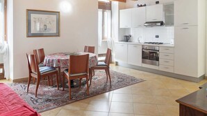 A modern kitchen with white cabinets, a stove, and a sink. There is a dining area with a table and chairs, and a rug on the floor. - Belvilla by OYO Vega (Caprino Veronese)
