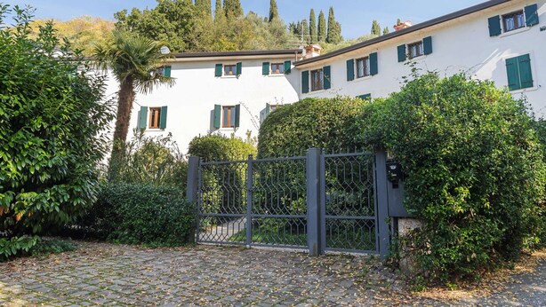 A white building with green shutters, surrounded by greenery and a cobblestone path. - Belvilla by OYO Vega (Caprino Veronese)
