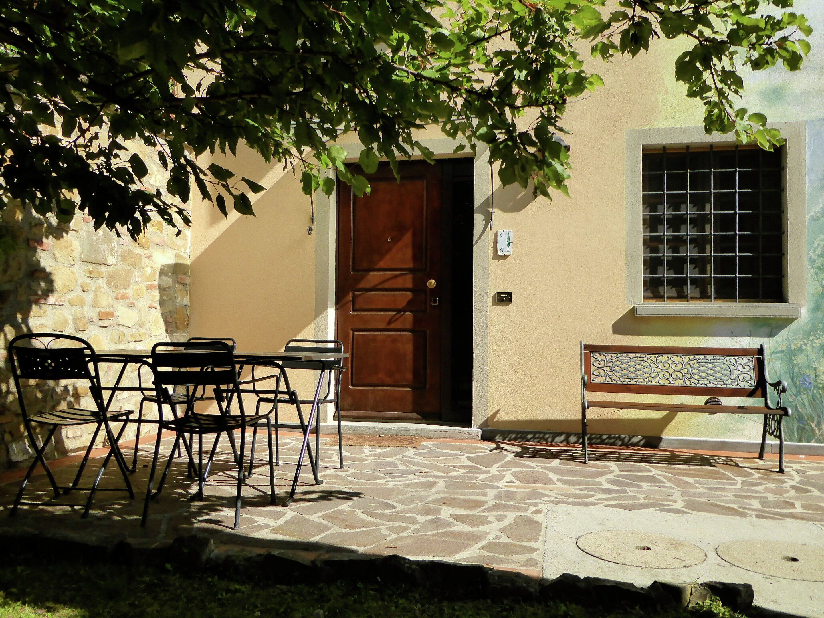 An outdoor seating area with a stone floor, a wooden door, and a window with a metal grid.