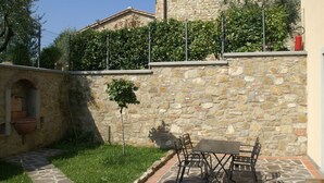 A stone building with a small garden area, a table with chairs, and a red fire extinguisher on the wall. - Holiday Home in Montecarelli With Pool (Barberino di Mugello)