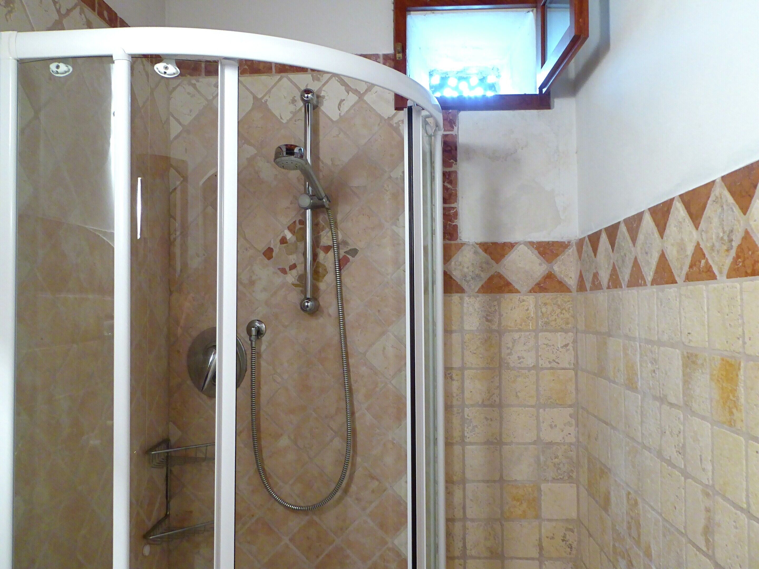 A glass-enclosed shower with a handheld showerhead and a wall-mounted faucet.