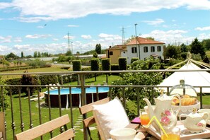 A balcony with a table set for breakfast, overlooking a swimming pool and a house. - Villa in Montecarlo With Pool and Scenic Views (Montecarlo)