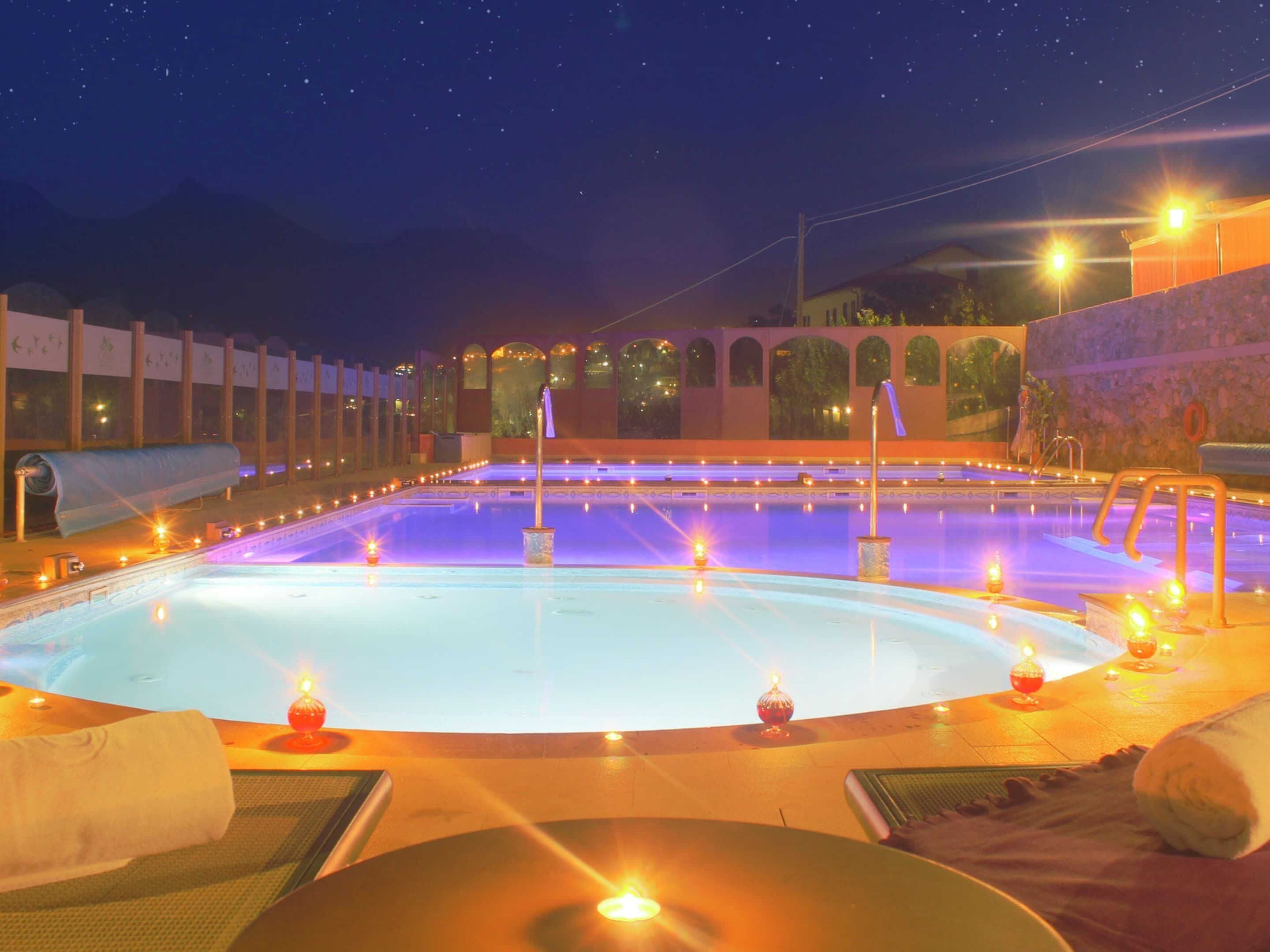 Una amplia piscina interior con varias pistas de natación, rodeada por un muro de piedra e iluminada por numerosas luces.