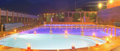 Una amplia piscina interior con varias pistas de natación, rodeada por un muro de piedra e iluminada por numerosas luces.