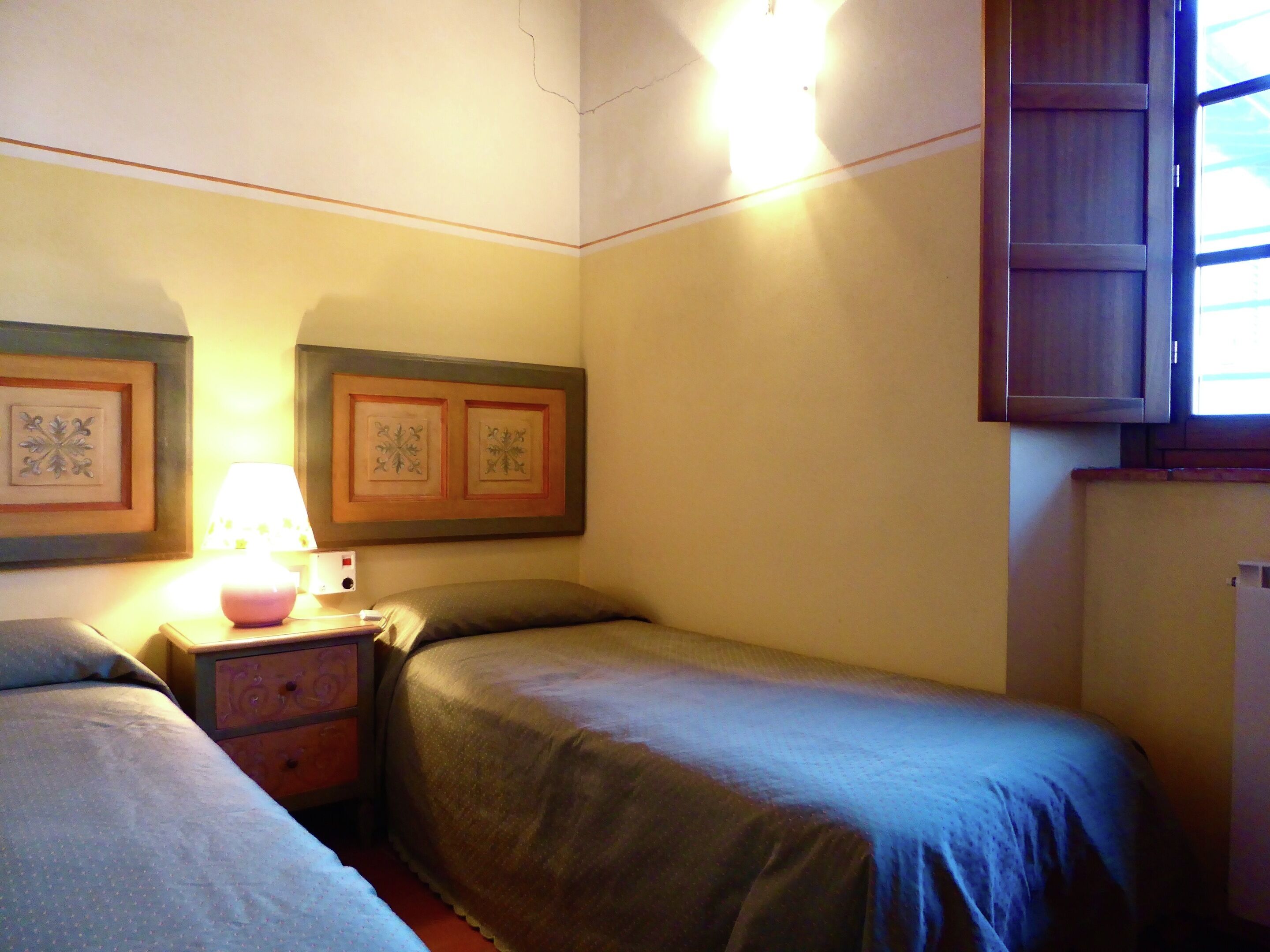 A bedroom with two single beds, a nightstand with a lamp, and a small cabinet.