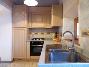 Une cuisine avec des meubles en bois, une cuisinière à gaz, un évier et un pare-feu en marbre.