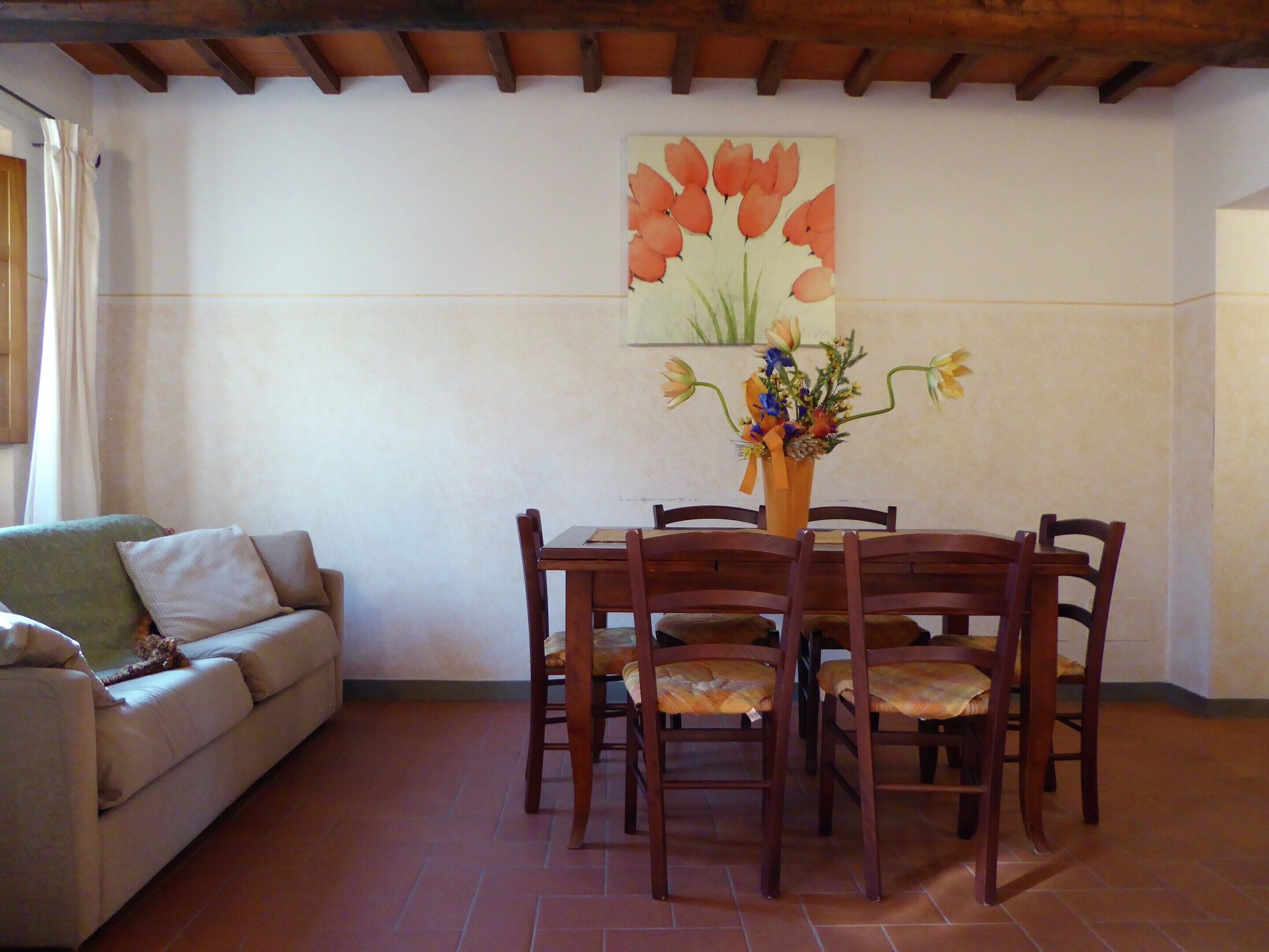 A dining area with a wooden table and chairs, a vase of flowers, and a painting of tulips on the wall.