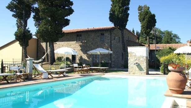 A pool area with lounge chairs and umbrellas, a stone building with a tiled roof, and a clear blue sky. - Holiday Home in Montecarelli With Pool (Barberino di Mugello)