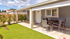 Une terrasse couverte avec une table et des chaises, une porte et une fenêtre avec des rideaux.