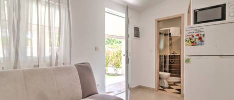 Un salon moderne avec un canapé, une porte donnant accès à une salle de bain et un réfrigérateur orné d’un autocollant.