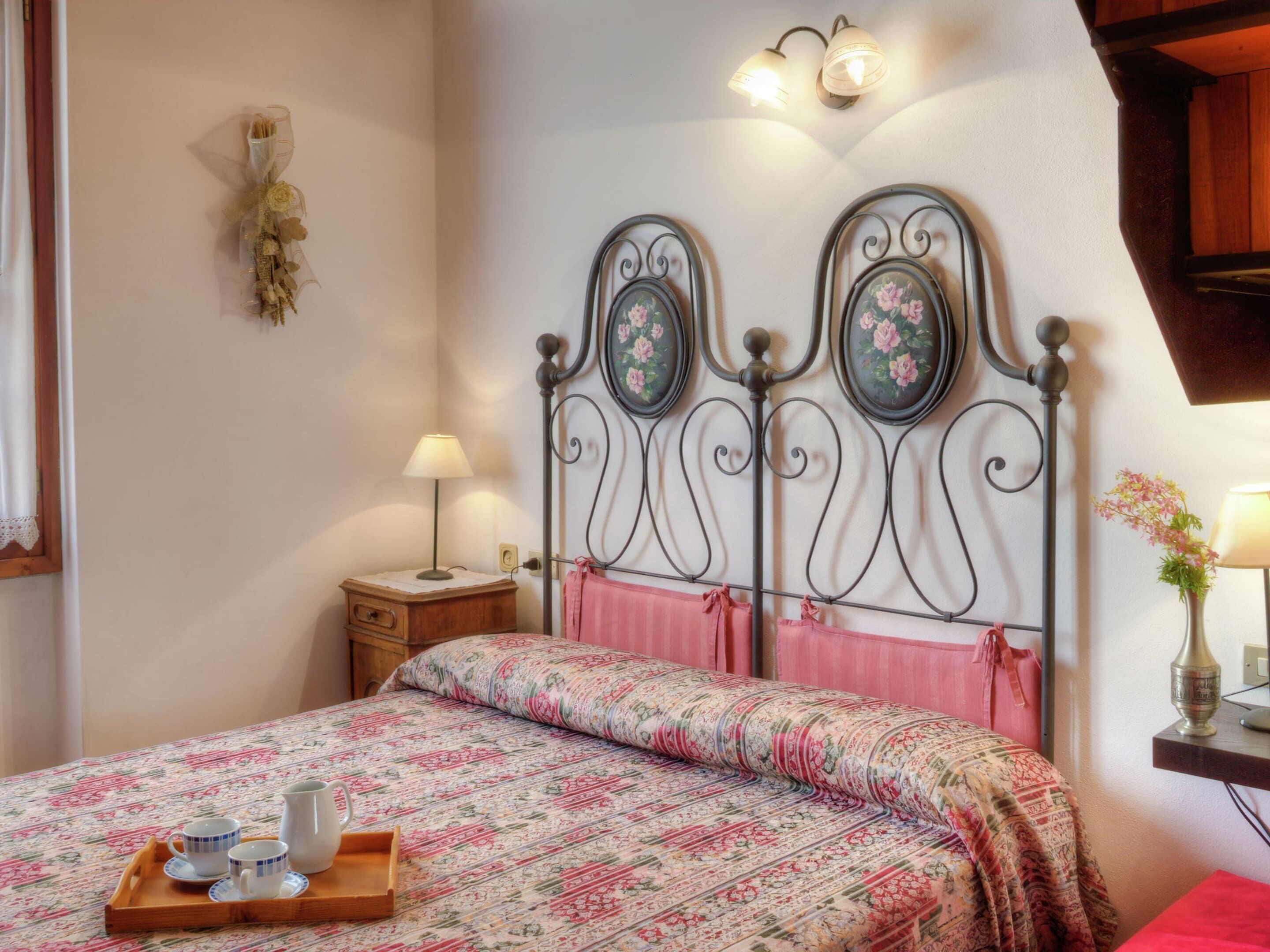 Un dormitorio con una colcha de estampado floral, una mesita de noche con una lámpara y un aplique de pared.