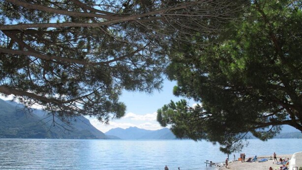 A lakeside view with a beach, people swimming, and mountains in the background. - Sunny & Peacefully Situated House near Center of Village (San Siro)