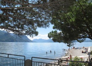 Une vue sur un lac, avec une plage, des gens qui se baignent et des montagnes en arrière-plan.
