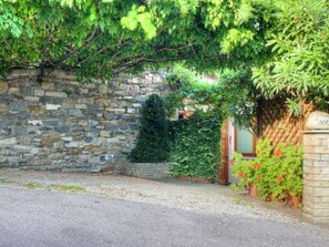 Eine Steinsäule mit einem hölzernen Torbogen, einem kleinen Baum und Topfpflanzen.