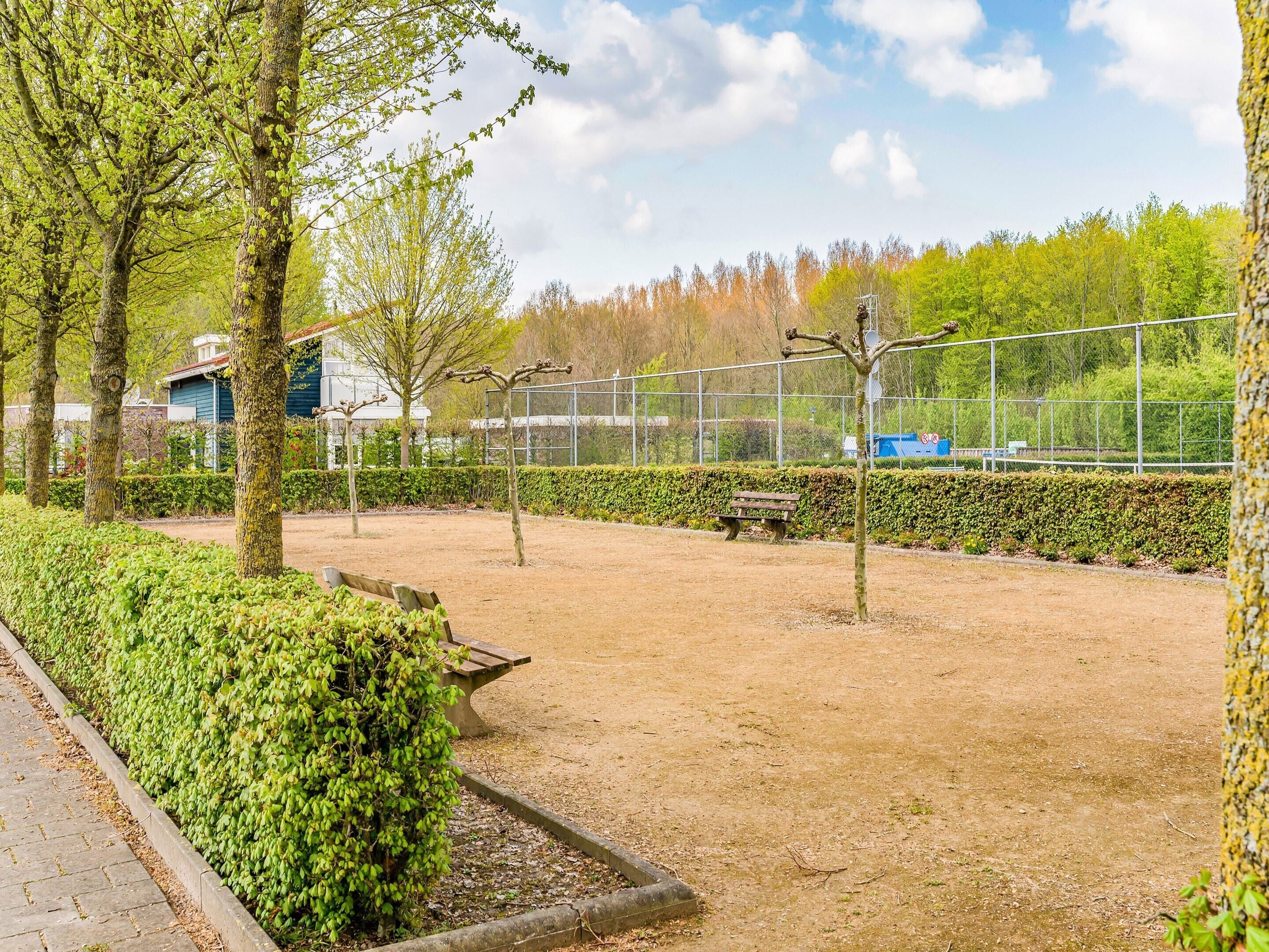 Un parc avec un sentier de terre, des bancs et une zone délimitée par une clôture.