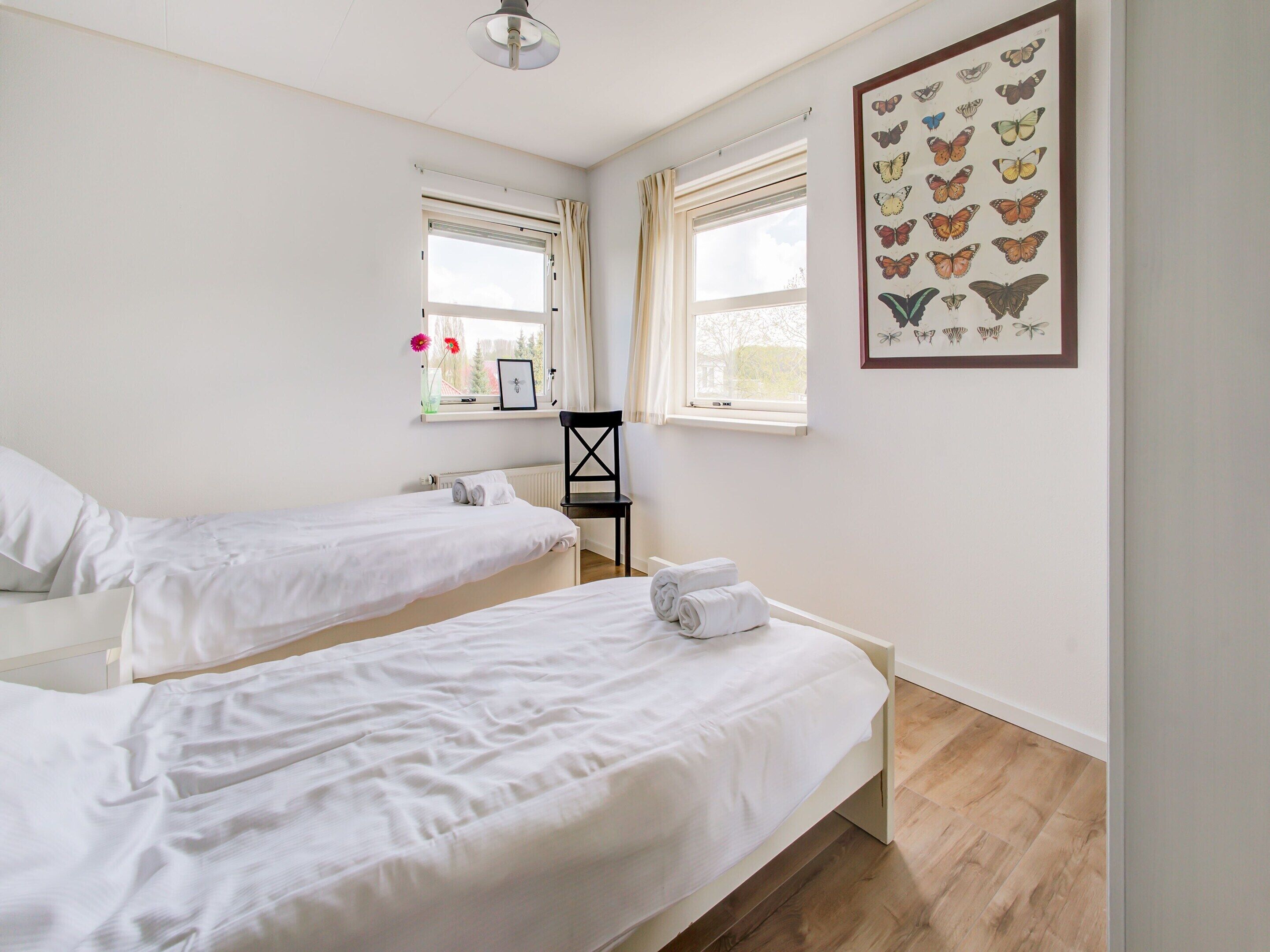 A room with two single beds, a black chair, a window with curtains, and a butterfly wall art.
