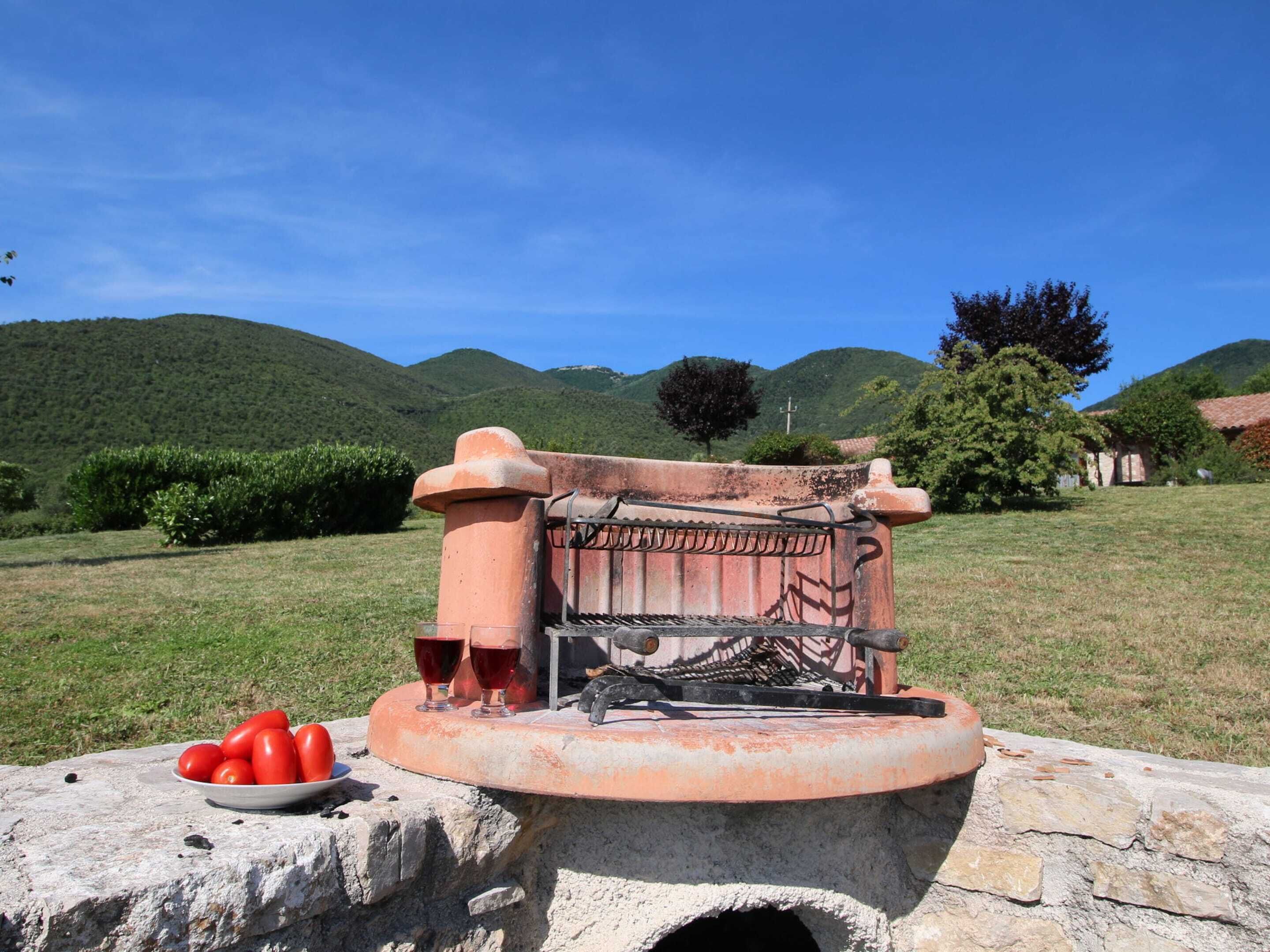 An outdoor water pump with a stone base, surrounded by a grassy field and hills in the background.