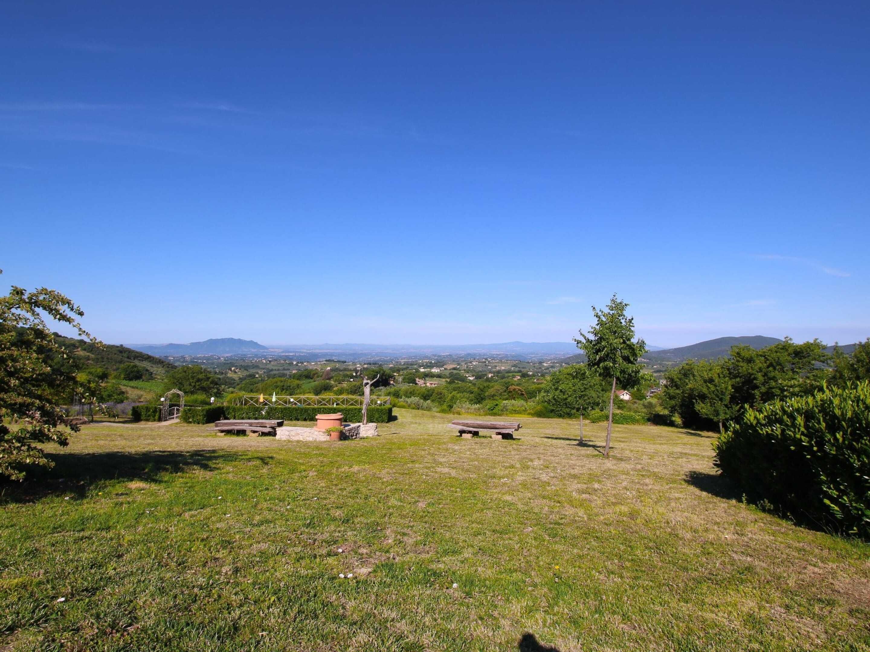 Un espace extérieur verdoyant, doté de tables de pique-nique et d’une pergola, qui offre une vue sur une vallée et des collines lointaines.